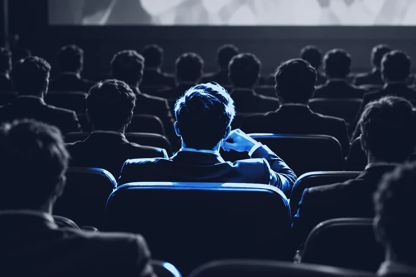 Siyah beyaz bir sinema salonunda, kalabalığın içinde mavi ışıkla aydınlanan tek izleyici